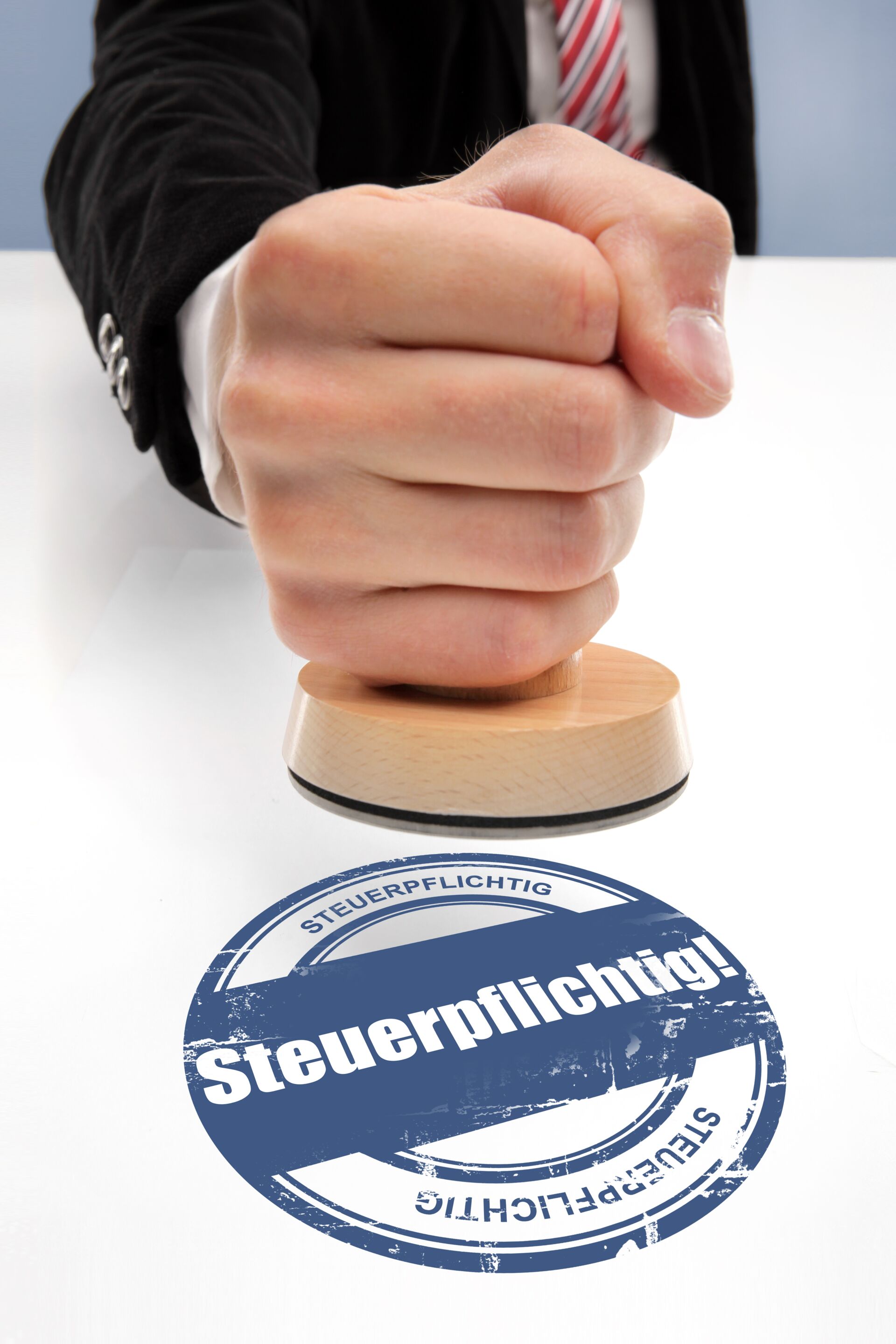 Eine geballte Faust drückt einen Stempel auf ein Papier, wo drauf steht "steuerpflichtig"
